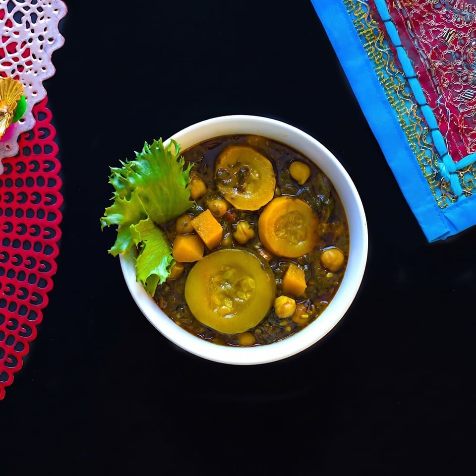 Overhead view of a bowl of dark green stew with yellow squash, chickpeas, and lettuce.