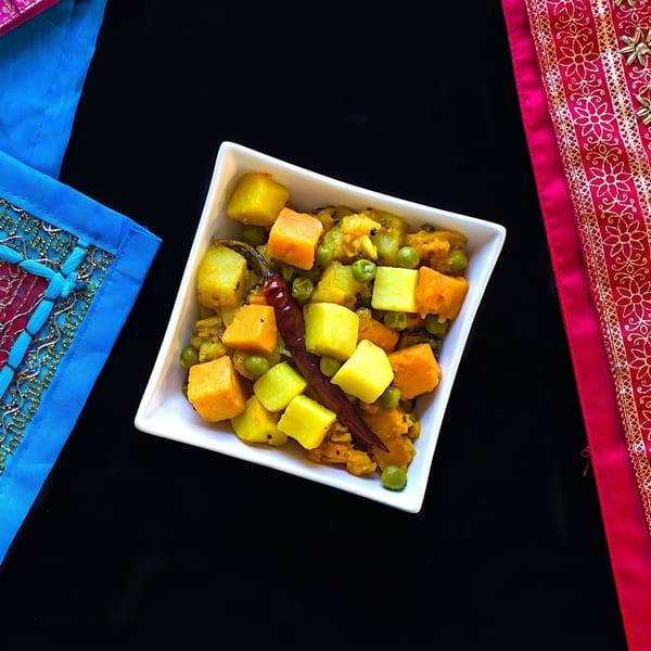 A white square bowl filled with colorful Indian vegetable curry, garnished with a red chili.