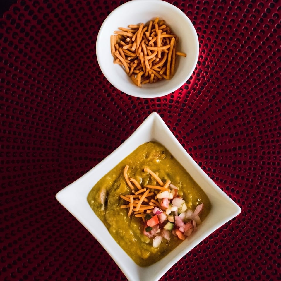Green curry with chopped onions and crunchy toppings, served with a side of crispy sticks.