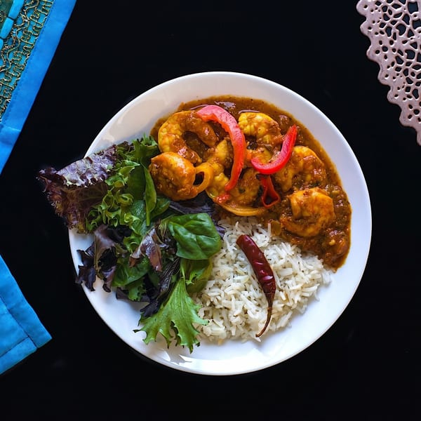 Shrimp curry with red bell peppers, white rice, a dried red chili, and mixed greens.