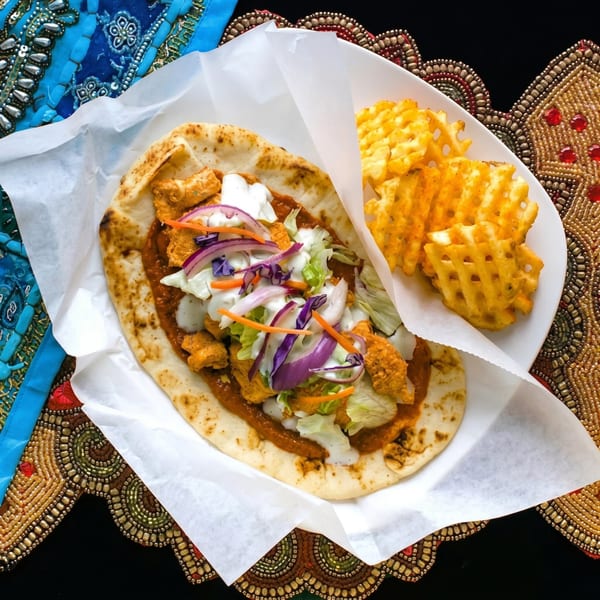 Chicken tikka naan wrap with waffle fries on a white plate with colorful embroidered fabric.