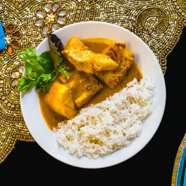 Curried fish with rice and a sprig of lettuce on a white plate, on a gold beaded placemat.