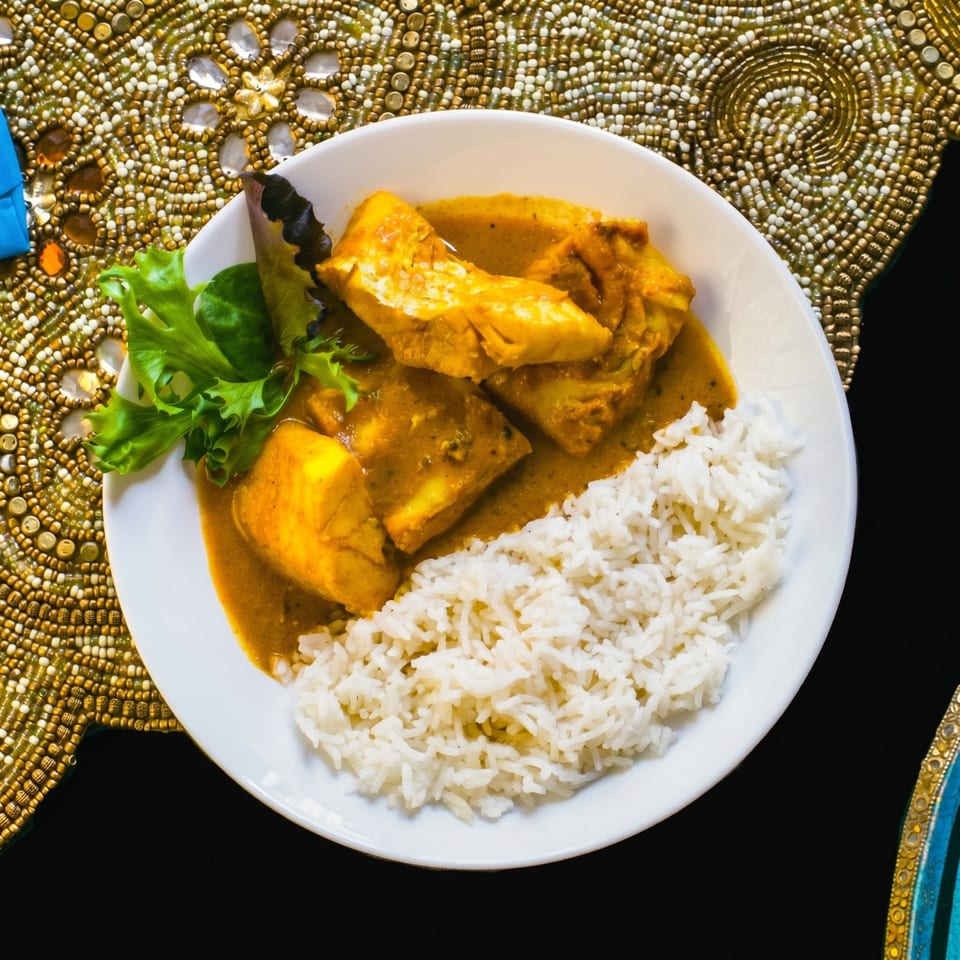 Curried fish with rice and a sprig of lettuce on a white plate, on a gold beaded placemat.