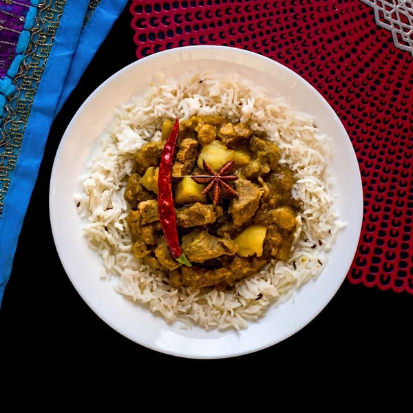 Curry with rice, red chili, and star anise on a white plate with colorful placemats.