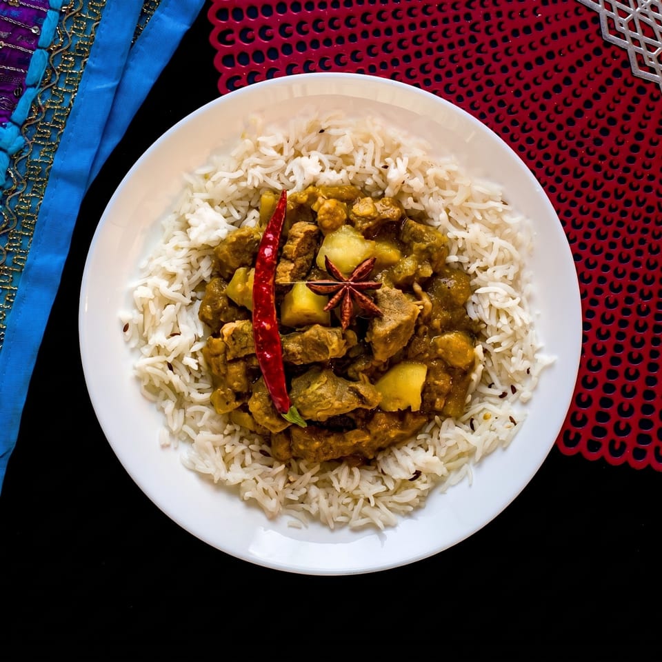 Curry with rice, red chili, and star anise on a white plate with colorful placemats.