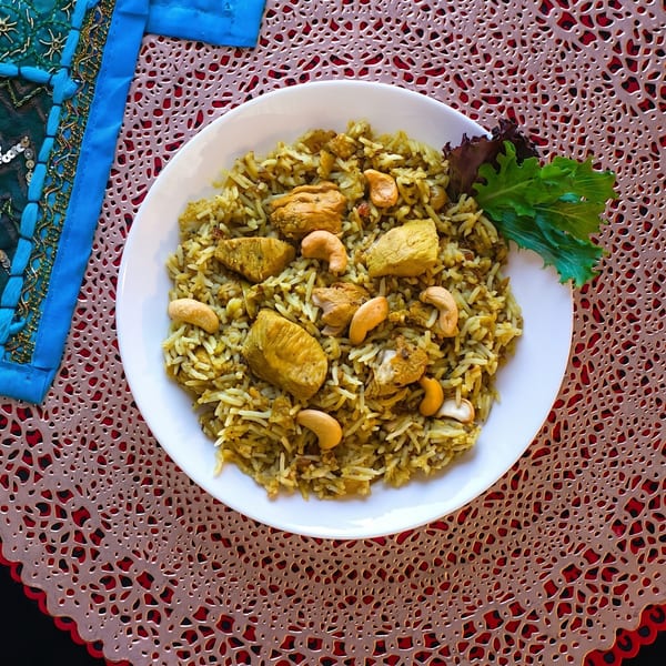 Chicken biryani with cashews and lettuce garnish on a white plate with a red placemat.